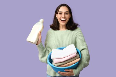 Çamaşır sepeti ve leylak arka planda bir şişe deterjanı olan genç bir kadın.