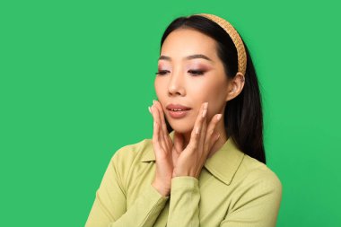 Yeşil arka planda pembe ruj sürmüş güzel Asyalı kadın.