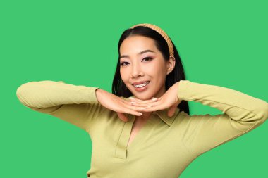 Yeşil arka planda pembe ruj sürmüş güzel Asyalı kadın.