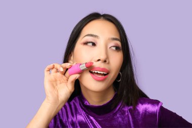 Leylak arka planına ruj süren güzel bir Asyalı kadın.