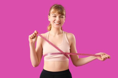 Güzel, genç ve sportif bir kadın, göğüslerini mor arka planda ölçüyor. Kilo verme konsepti