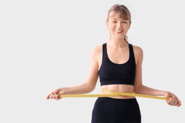 Gri arka planda belini ölçen genç ve güzel bir kadın. Kilo verme konsepti