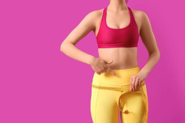 Mor arka planda kalçalarını ölçen genç, sportif bir kadın. Kilo verme konsepti