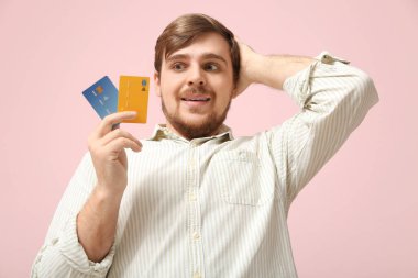 Pembe arka planda kredi kartları olan korkmuş genç bir adam.