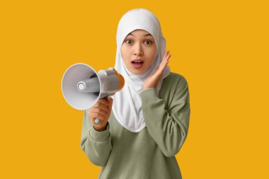 Sarı arka planda megafonla genç Asyalı Müslüman kadını şok etti. Ulusal Duyulma Günü