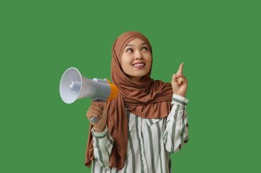 Yeşil arka plandaki bir şeyi işaret eden megafonlu genç Asyalı Müslüman kadın. Ulusal Duyulma Günü