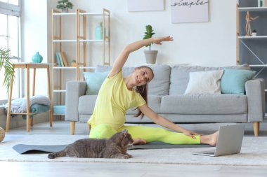 Kedi ve dizüstü bilgisayarlı hamile bir kadın evde yoga yapıyor.