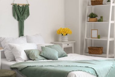 Hafif yatak odasındaki masanın üzerinde nergisler olan vazo.