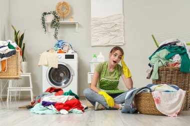Çamaşır makinesinin yanında kirli çamaşırları olan yorgun genç bir kadın.