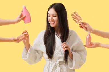 Bornozlu genç Asyalı kadın ve sarı arka planda saç ürünleri olan eller.