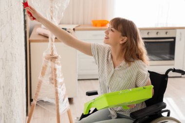 Tekerlekli sandalyede duvarları boyayan genç bir kadın.