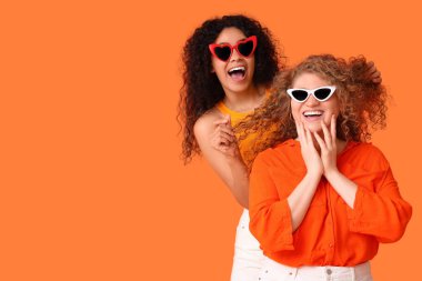 Turuncu arka planda güneş gözlüklü güzel genç kadınlar.
