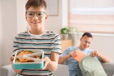 Gözlüklü küçük çocuk okulda beslenme çantası takıyor.