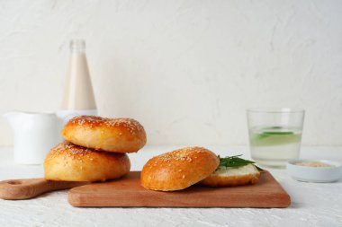 Wooden board of tasty bagels with butter and arugula on white background clipart