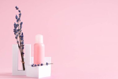 Dekoratif podyumlar, bir şişe kozmetik ürünü ve pembe arka planda lavanta çiçekleri.