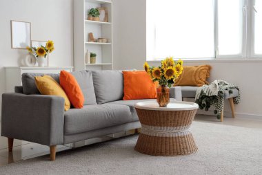 Gri kanepeli şık bir oturma odası ve kahve masasında ayçiçeği buketleri.