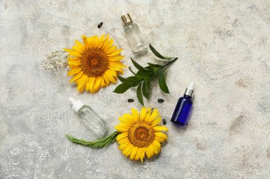 Esaslı yağ şişeleri, ayçiçekleri ve grunge arkaplanındaki bitki dallarıyla kompozisyon