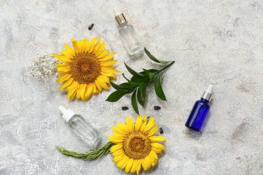 Esaslı yağ şişeleri, ayçiçekleri ve grunge arkaplanındaki bitki dallarıyla kompozisyon