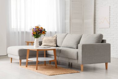 Oturma odasının içindeki sehpada yabani çiçekler olan rahat bir kanepe ve vazo.