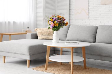 Oturma odasının içindeki sehpada yabani çiçekler olan rahat bir kanepe ve vazo.