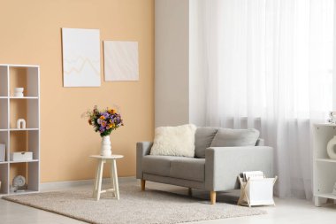 Oturma odasındaki sehpanın üzerinde yabani çiçekler olan kanepe, raf ünitesi ve vazo.