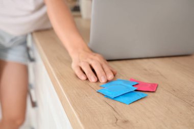 Dizüstü bilgisayarı ve prezervatifleri olan genç bir kadın mutfaktaki masada, yakın plan.