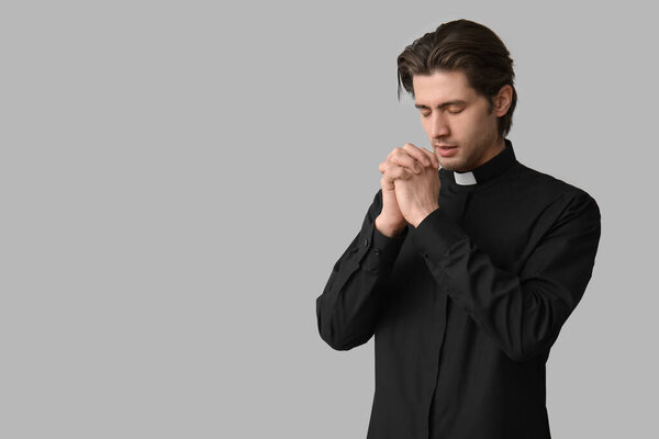 Молодой священник молится на тёмном фоне