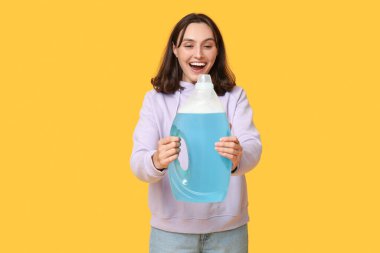 Sarı arka planda deterjan şişesi olan genç bir kadın.