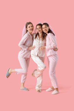 Pembe arka planda pijamalı nedimeleri olan genç bir kadın. Kız Partisi