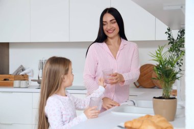 Küçük kızı mutfakta bardak yıkarken mutlu bir anne.