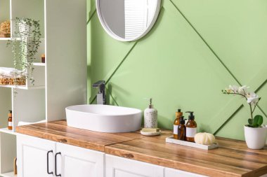 Banyonun içinde raf ünitesi, çekmeceler ve yeşil duvarın yanında lavabo var.