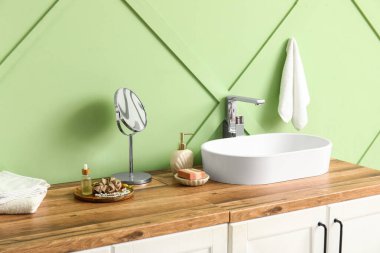 Banyoda yeşil duvarın yanında banyo malzemesi ve lavabo olan çekmeceler.