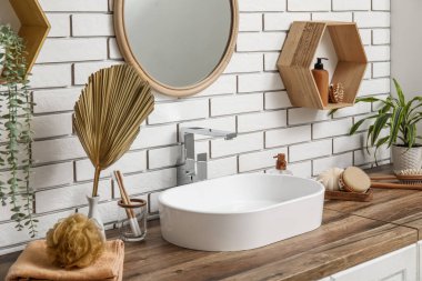 Banyodaki beyaz tuğla duvarın yanındaki çekmecelere lavabo ve banyo malzemeleri.