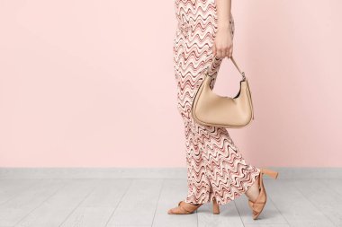 Pembe duvarın yanında çantalı, şablon pantolonlu, topuklu ayakkabılı şık bir genç kadın.