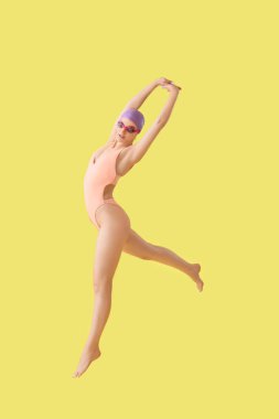 Sarı arka planda atlayan profesyonel genç bayan yüzücü.