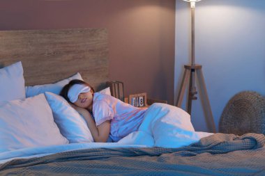 Maskeli genç ve güzel bir kadın geceleri yatak odasında uyuyor.