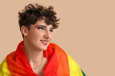 Bej arka planda LGBT bayrağı olan genç transseksüel kadın, yakın plan.