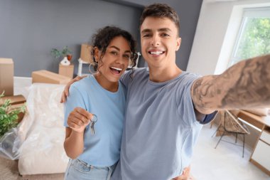 Yeni evlerinin anahtarlarını taşıyan genç çift taşınma gününde odada selfie çekiyorlar.