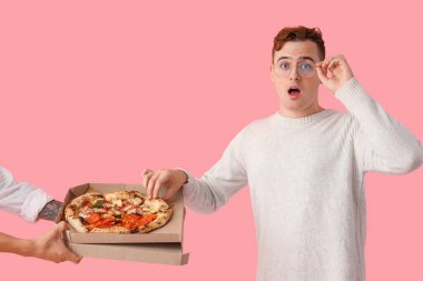 Genç adam pembe arka planda lezzetli pizzalar yiyor.