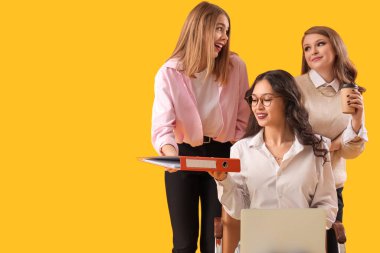 Young women gossiping behind their colleague's back on yellow background