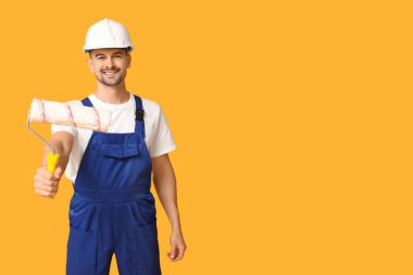 Sarı arka planda boya silindirli erkek ressamın portresi