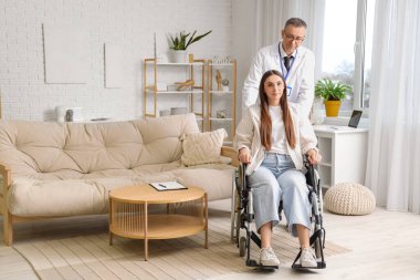 Evde tekerlekli sandalyede genç bir kadın olan olgun bir doktor.