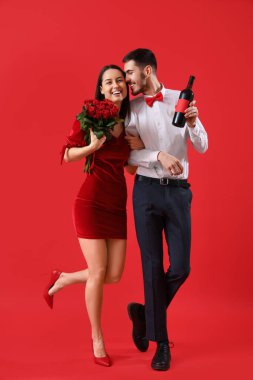 Kırmızı arka planda şarap ve gülleri olan mutlu genç bir çift. Sevgililer Günü kutlaması