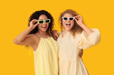 Sarı arka planda güneş gözlüklü güzel genç kadınlar.