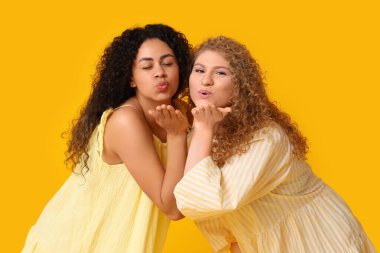 Güzel genç kadınlar sarı arka planda öpüşüyorlar