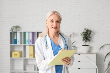 Olgun kadın doktor hastanede panoya yazı yazıyor.