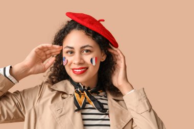 Beautiful young happy African-American woman with USA and France flags on her face against beige background clipart