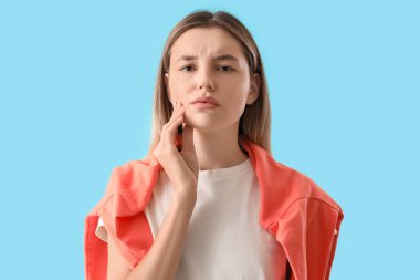 Mavi arka planda diş ağrısı çeken genç bir kadın.