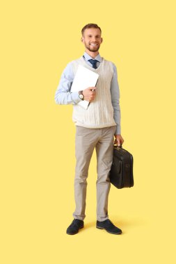 Sarı arka planda dizüstü bilgisayarı ve çantası olan genç bir iş adamı.