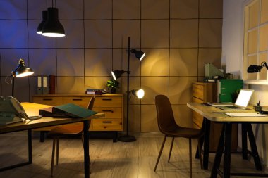 Masaları ve parlak lambaları olan karanlık ofisin içi.